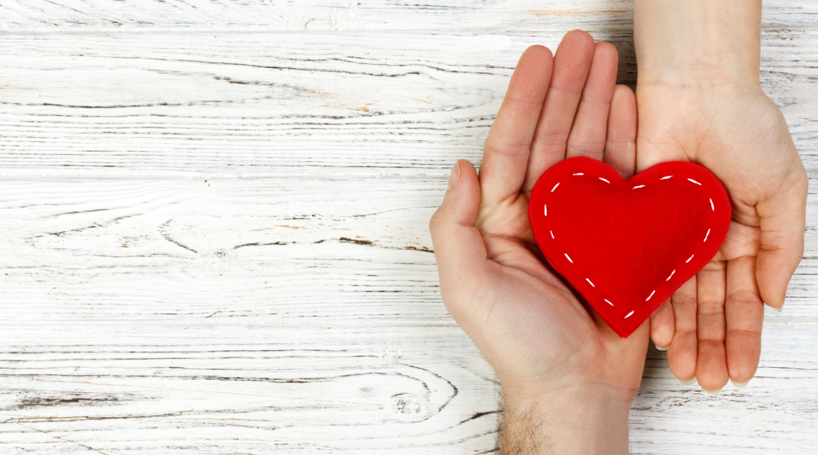 Two outstretched arms holding a heart shaped object in hand.