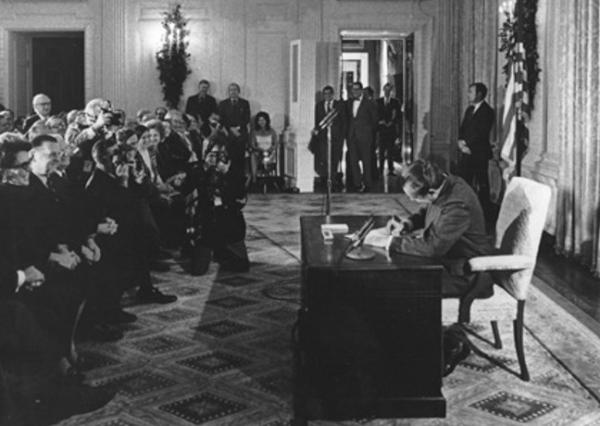 A historical picture of President Nixon seated at a desk, signing the National Cancer Act