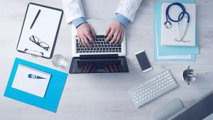 Image of clinician's hands typing on laptop on office desk from above.