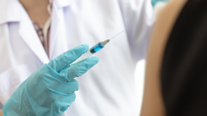 A medical assistant holding a syringe with a gloved hand.