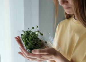 A picture of a woman holding a container full of broccoli sprouts.