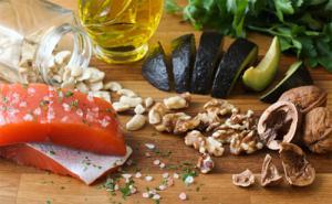 Healthy foods displayed on a table, including salmon, garlic, avocado, and walnuts.