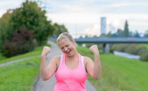 An picture of a woman wearing a pink top, giving a celebratory fist pump above her head.