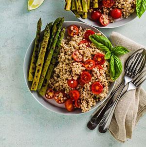 A bowl of sorghum with tomatoes and asparagus.