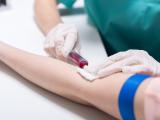 An image of a patient's arm with a blue tourniquet and nurse, arm and part of her body visible only, drawing blood.