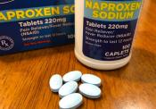 A bottle of Naproxen placed atop a table with some tablets displayed.