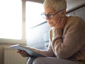 An older woman reading a tablet.