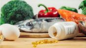 An open bottle of Vitamin D on a table with eggs, fish, and vegetables.