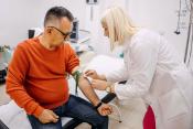 A middle-aged man sitting on a hospital bed having his blood drawn by a medical technologist.